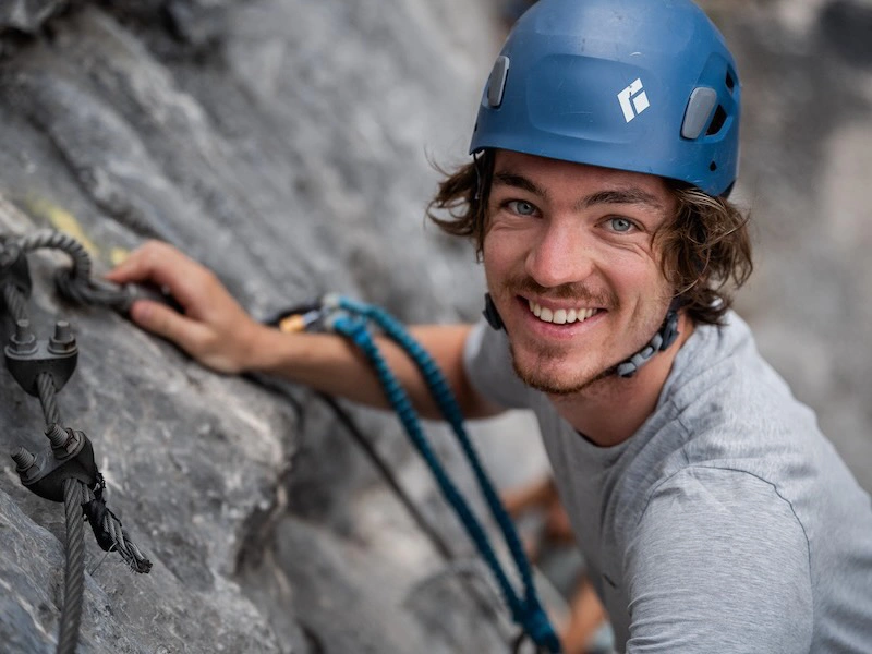 Participant souriant équipé sur une paroi rocheuse lors de la Via Ferrata La Panoramique à Saint-Paul-de-Fenouillet.