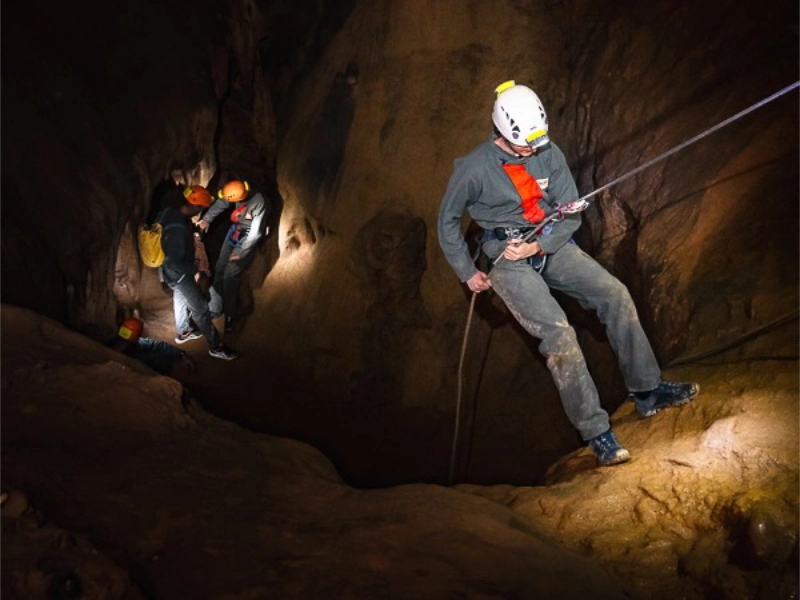 Spéléologue descendant en rappel dans une grotte des gorges de Galamus avec un groupe lors d’une sortie spéléologie dans les Pyrénées-Orientales