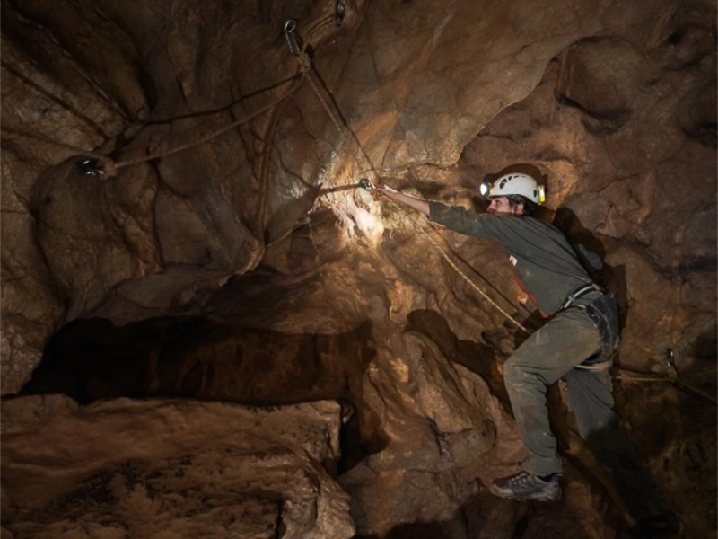 Spéléologue franchissant un passage technique sur corde dans une grotte des gorges de Galamus dans les Pyrénées-Orientales
