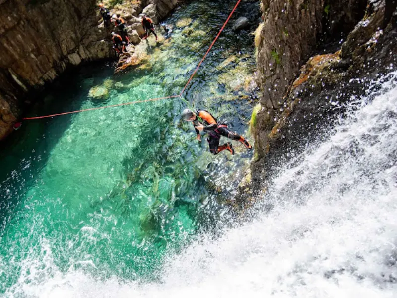 Participant sautant dans une vasque turquoise du canyon de l’Artigue en Ariège lors d’une sortie canyoning dans la vallée de Vicdessos