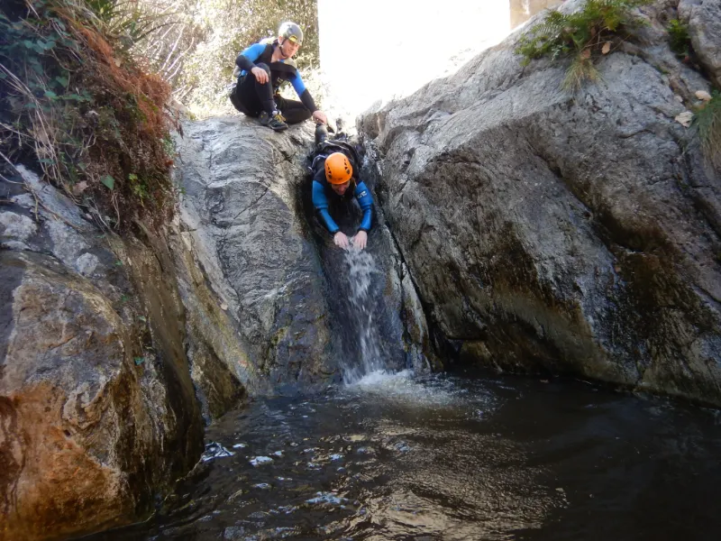 Participant glissant dans un toboggan naturel lors d’une sortie canyoning dans le canyon d’eau chaude de Thuès près de Font-Romeu dans les Pyrénées